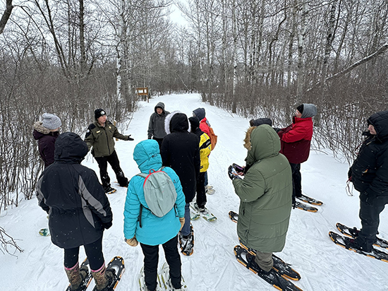 Session instructor teaches snowshoe course to group of women on winter trail