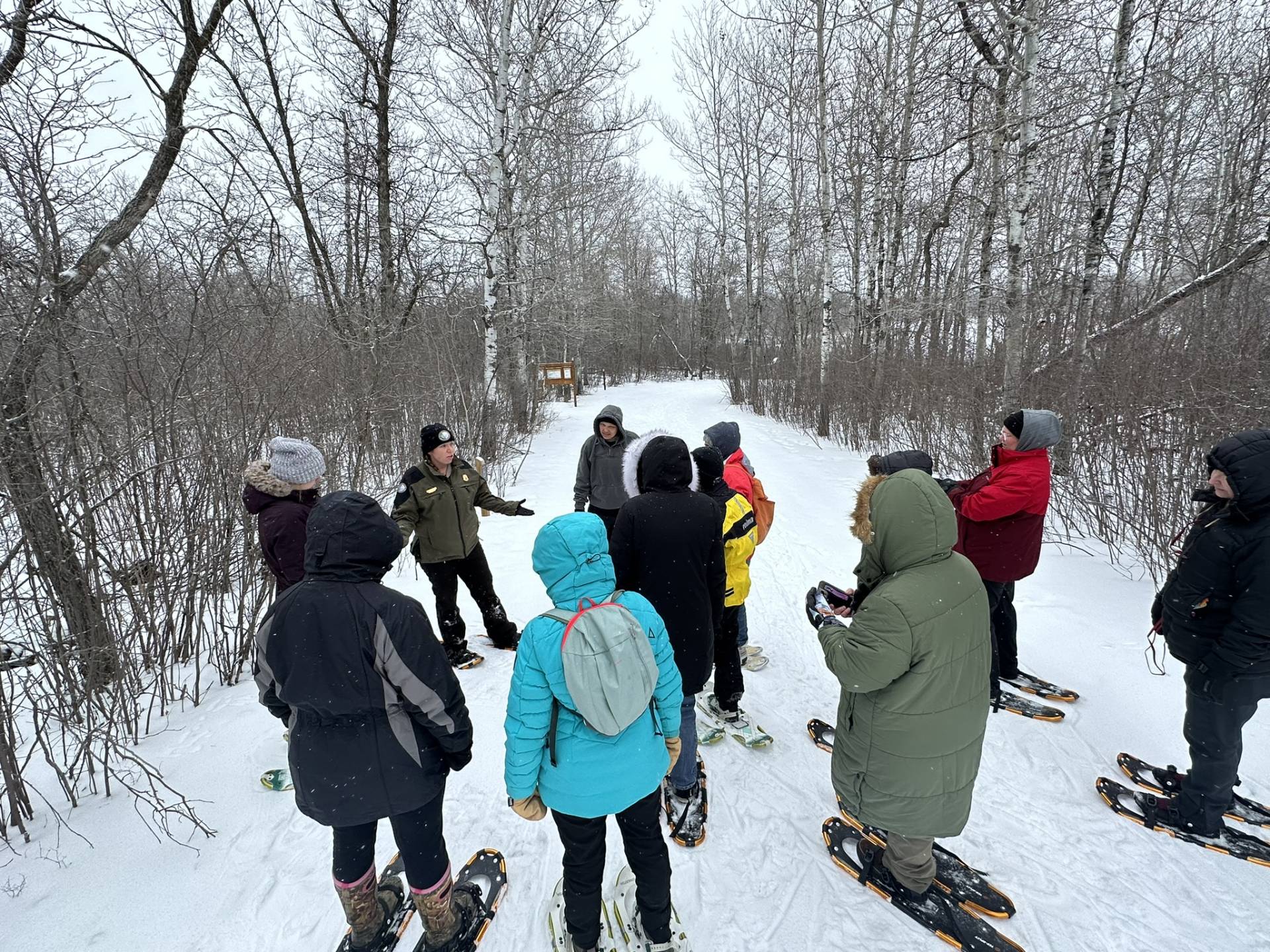 Session leader teaches women on snowshoes on snowy, wooded trail