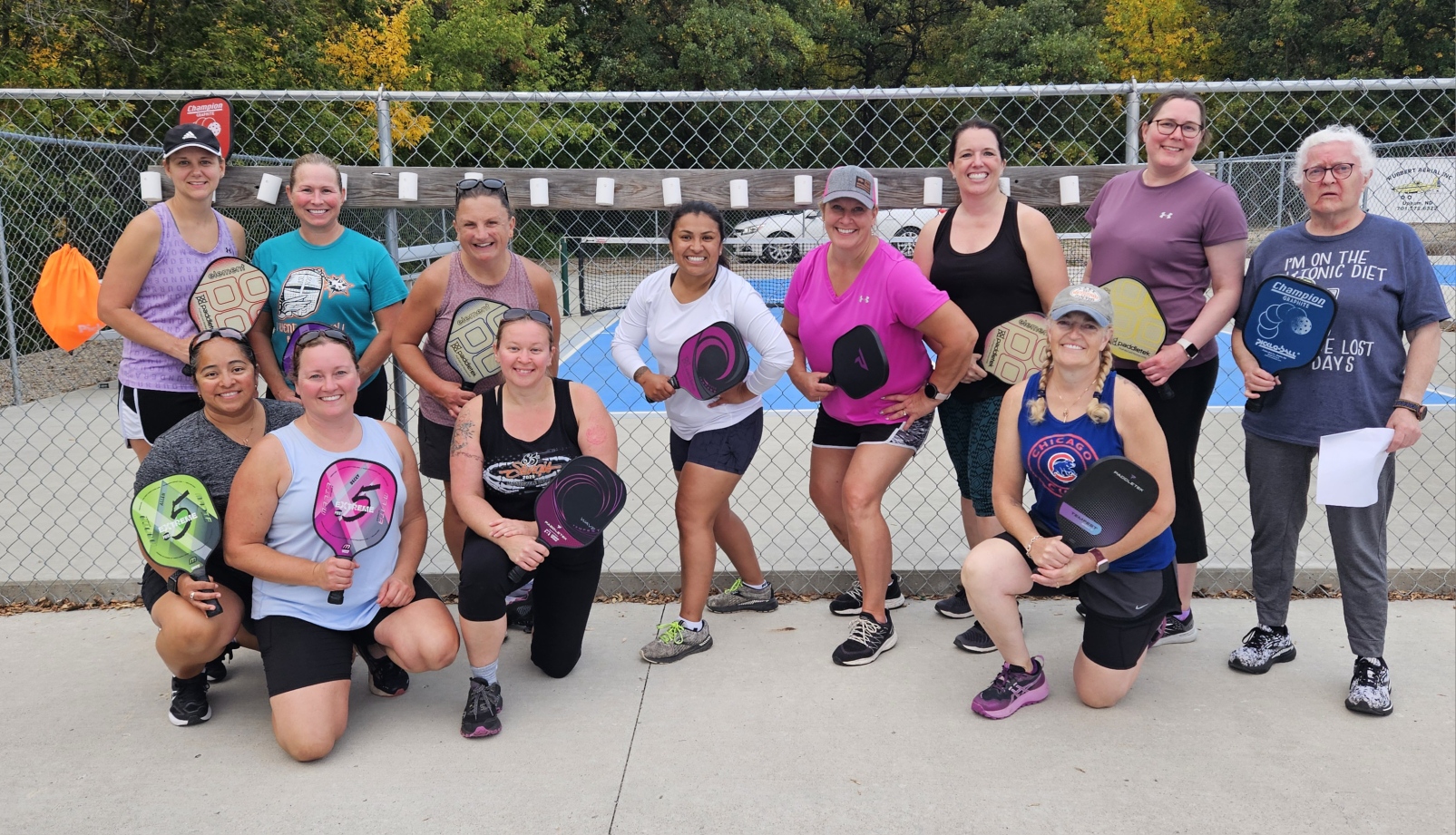 Group of smiling women pose while playing pickleball