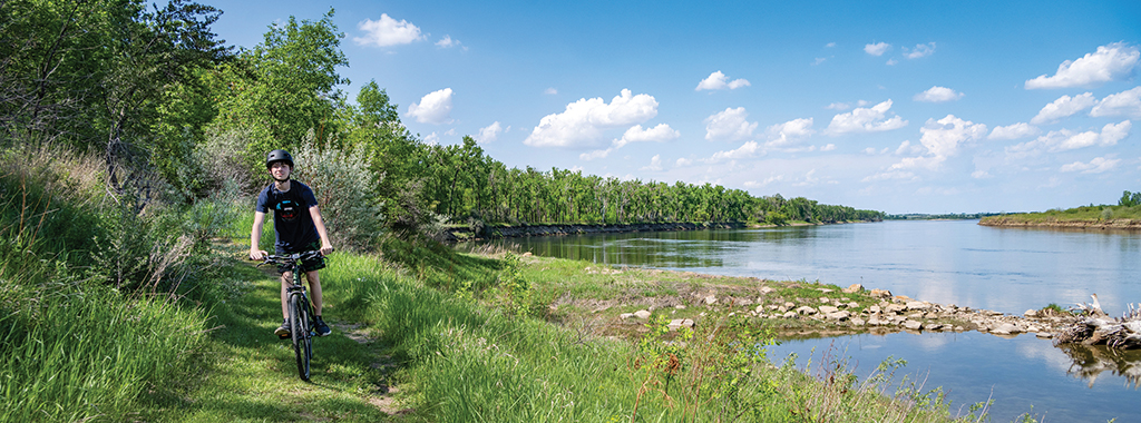A young boy riding bike on a path by a river.