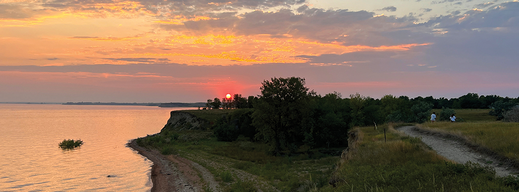 Cliff edge with a path overlooking the lake under a colorful sunset.