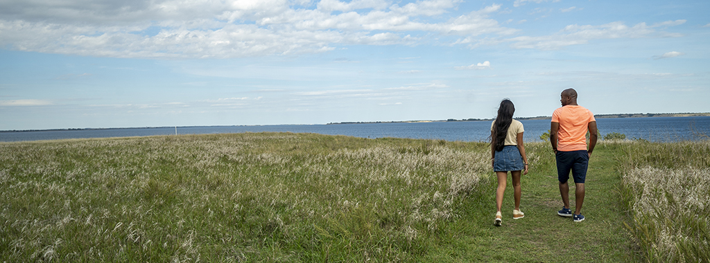 two people walking on a path in a field toward a lake in the distance.