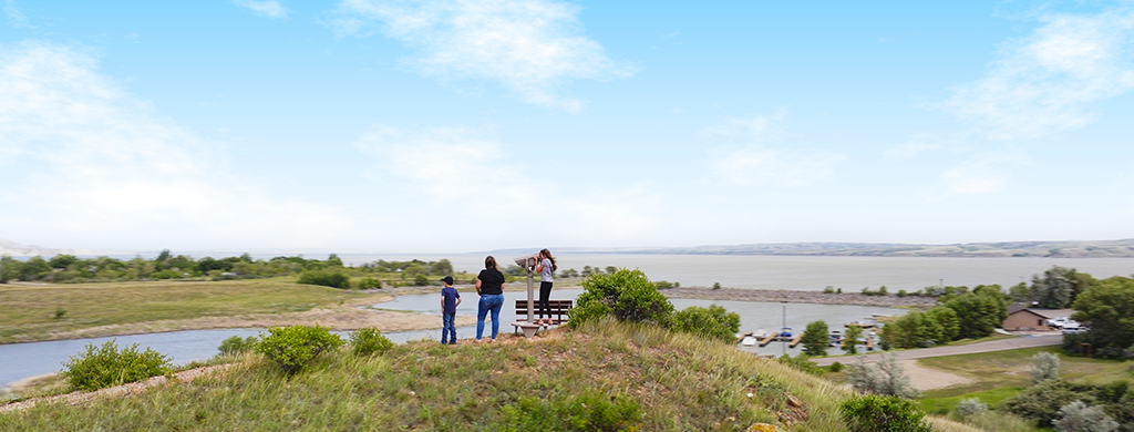 Three people standing on a hilltop overlooking a lake.