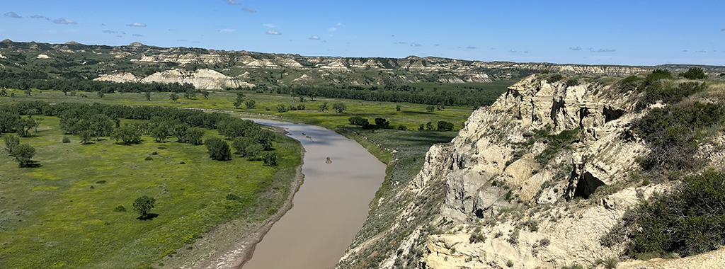 A river flowing through a lush green landscape and The Badlands in the distance.